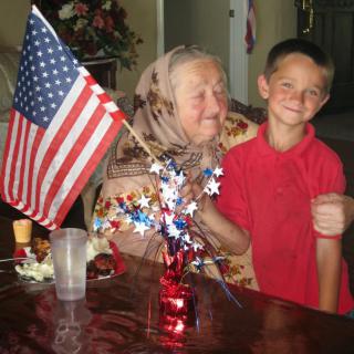 An elderly woman and a young boy smiling with an American flag decoration on the table.