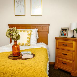 A cozy bedroom with a single bed adorned with a yellow blanket, next to a wooden nightstand.