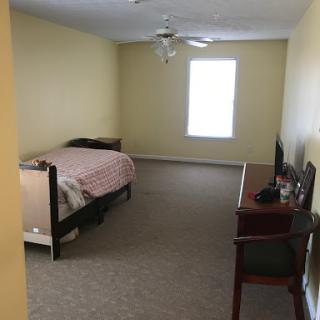 A simple and spacious bedroom with a bed, desk, and window.