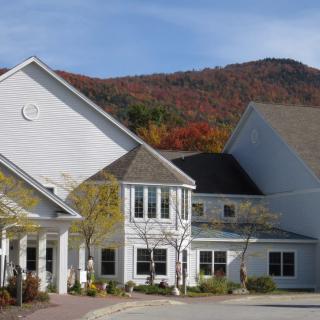 A large white house set against a mountain backdrop with autumn foliage.