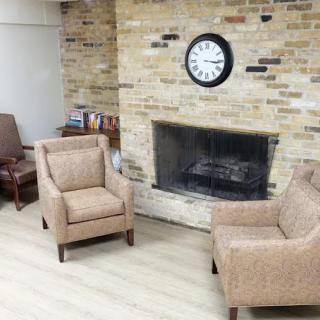 A cozy seating area featuring a brick fireplace, two armchairs, and a clock on the wall.