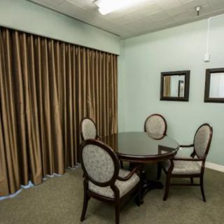 A small, simple room with a round table and four chairs, featuring brown curtains and mirrors on the wall.