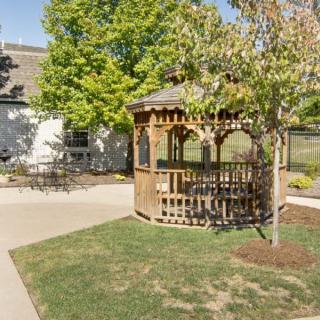 Charming garden gazebo surrounded by lush greenery next to a pathway and building.