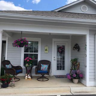 A cozy porch with chairs, flowers, and hanging plants.