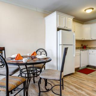 A cozy kitchen and dining area featuring a round table set for four, with a refrigerator and dishwasher in the background.