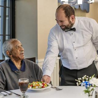 A waiter serves a meal to an elderly person at a restaurant.