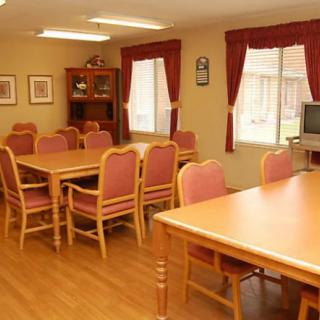 A cozy dining room with wooden tables and chairs, featuring large windows with red curtains.