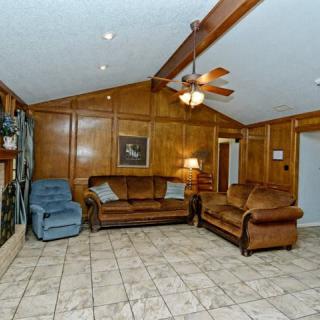 A cozy living room with wood paneling, featuring a ceiling fan, two leather sofas, a recliner, and tiled flooring.