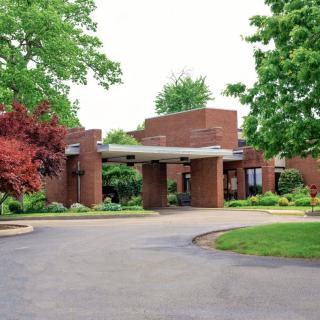 A brick building entrance surrounded by landscaped greenery and a curved driveway.