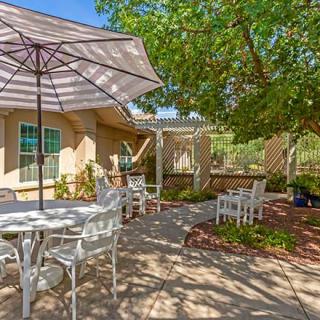 A cozy outdoor patio area with tables, chairs, and a large umbrella in a garden setting.