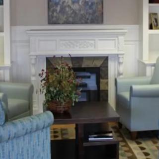 A cozy living room with a white fireplace, surrounded by armchairs and a coffee table.