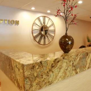 A reception area featuring a marble desk, decorative clock, and flower vase.