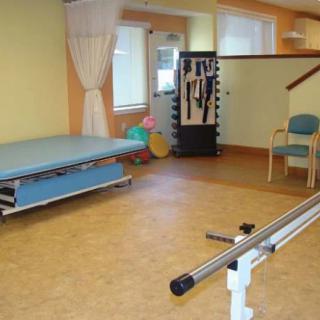 A physical therapy room equipped with a therapy bed, parallel bars, and exercise equipment.