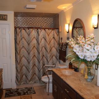 A well-decorated bathroom featuring a patterned shower curtain, a wooden vanity with a large mirror, and elegant lighting fixtures.