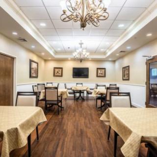 An elegant dining room with chandeliers, neatly arranged tables and chairs, and a polished wooden floor.