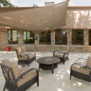 A cozy outdoor patio setup with cushioned chairs arranged around a fire pit, shaded by a canopy.