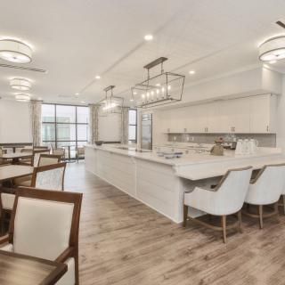 A spacious, modern kitchen with an island counter and dining area, featuring elegant chandeliers and wood flooring.