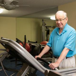 An elderly person standing on a treadmill in a gym setting.