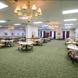 A spacious dining room with arranged tables and chairs, featuring chandeliers and a carpeted floor.