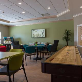 A community recreation room with tables, chairs, and a shuffleboard table.