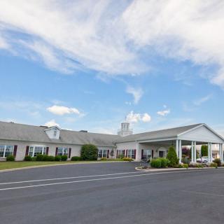 A single-story building with a large parking area, set against a blue sky with scattered clouds.