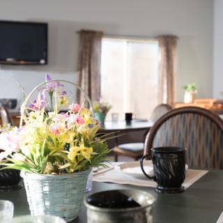 A cozy dining space illuminated by natural light, featuring a floral centerpiece and a coffee mug on the table.