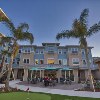 A modern residential building with palm trees and outdoor seating.