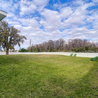 A spacious grassy yard with a tree, bordered by a fence under a partly cloudy sky.