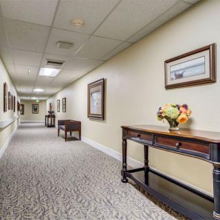 A well-lit hallway with tables, artwork, and carpeted flooring.