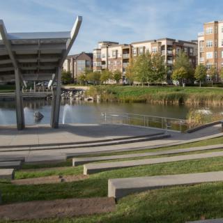 A modern amphitheater overlooking a tranquil lake with residential buildings in the background.