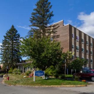 A hospital building surrounded by trees under a blue sky with clouds.