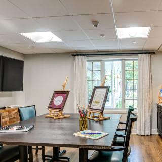 A well-lit meeting room featuring a large table, several chairs, and easels displaying artwork by the window.