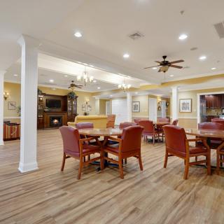 A spacious and elegantly designed dining area with multiple tables and chairs, featuring wooden flooring, ceiling fans, and ambient lighting.