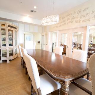An elegant dining room with a long wooden table, upholstered chairs, and a chandelier.