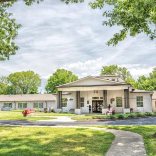 A picturesque view of a building with a welcoming entrance, surrounded by trees and a well-maintained lawn.