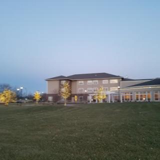 A modern building set against the evening sky, surrounded by lush green grass and illuminated trees.