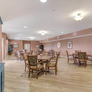 A spacious dining room with multiple tables and chairs, decorated with wall art and illuminated by ceiling lights.