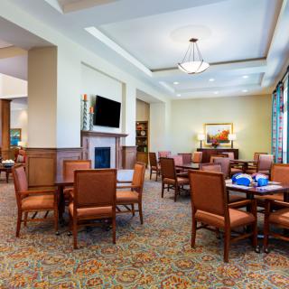 A spacious and well-lit dining room with several tables and chairs, featuring a television and elegant decor.