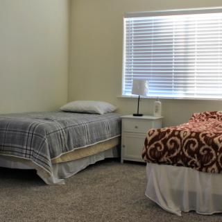 A simple bedroom with two twin beds, a nightstand, and a window.