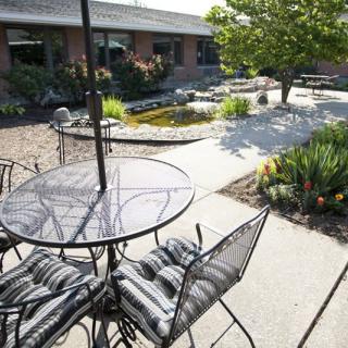 A sunny outdoor patio with a metal table and chairs, surrounded by lush garden landscaping.