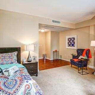 A cozy bedroom with colorful decor, featuring a bed with patterned bedding, a side table with a lamp, and a comfortable chair in the corner.