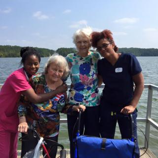 A group of people, including elderly individuals and caregivers, enjoying time by the lake.