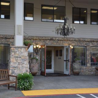 The entrance of a building featuring a stone facade, an outdoor bench, potted plants, and a chandelier.