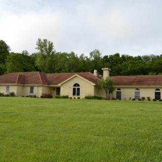 A spacious one-story house with a large lawn and surrounding trees.