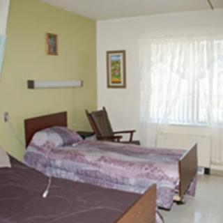 A simple bedroom with two beds, a chair, and a window.
