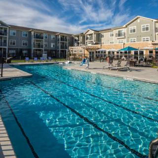 A spacious outdoor swimming pool surrounded by modern apartment buildings on a sunny day.