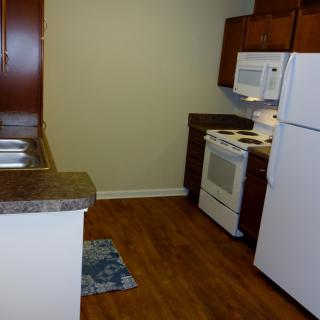 A compact kitchen with wooden flooring, featuring a refrigerator, microwave, and oven.
