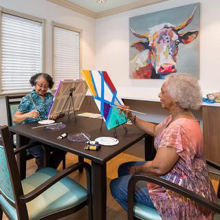 Two senior women enjoying a painting session together indoors.
