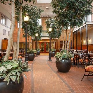 A spacious indoor restaurant area featuring tall potted trees and a brick floor.