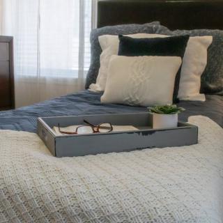 A neatly arranged bed with decorative pillows and a tray holding glasses and a small plant.